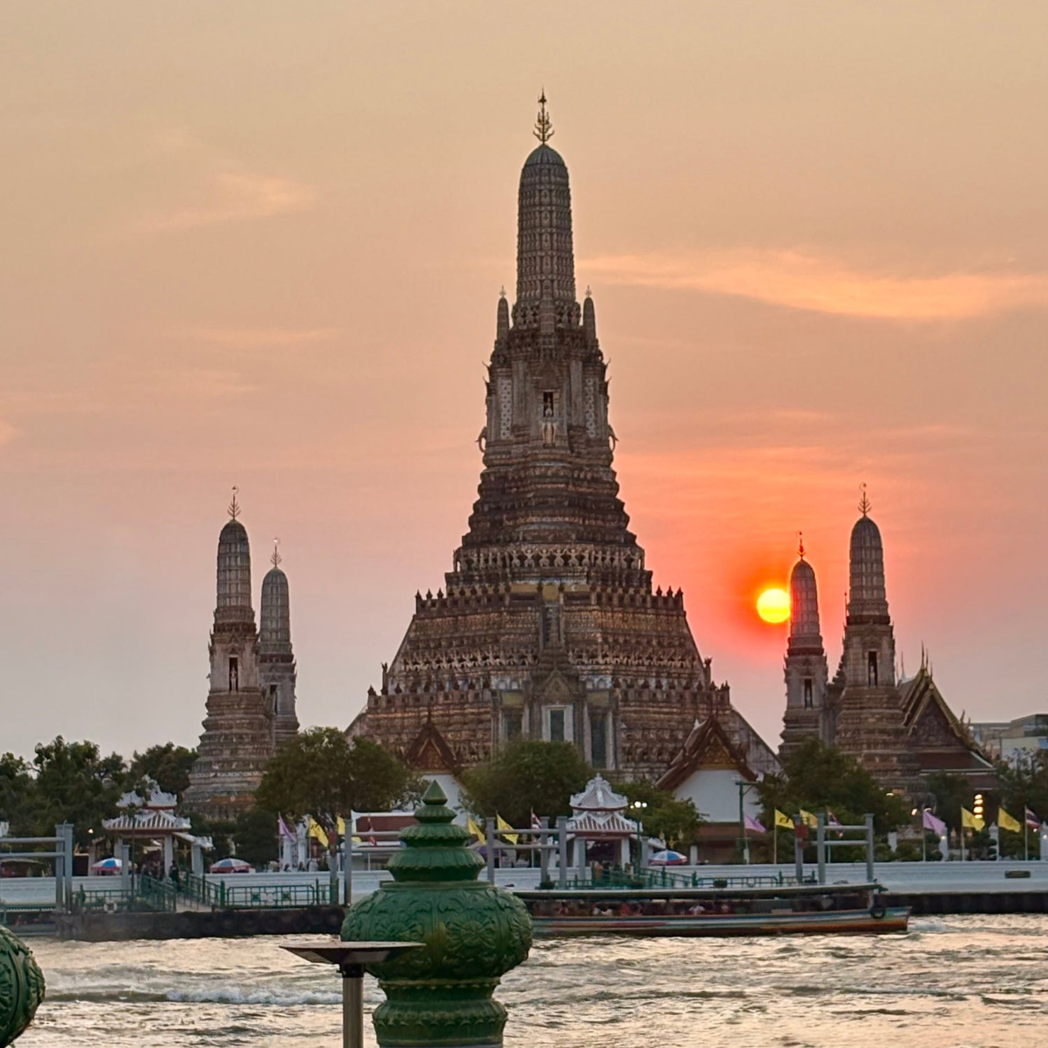 Wat Arun temple at sunset with a pink sky and water in the foreground