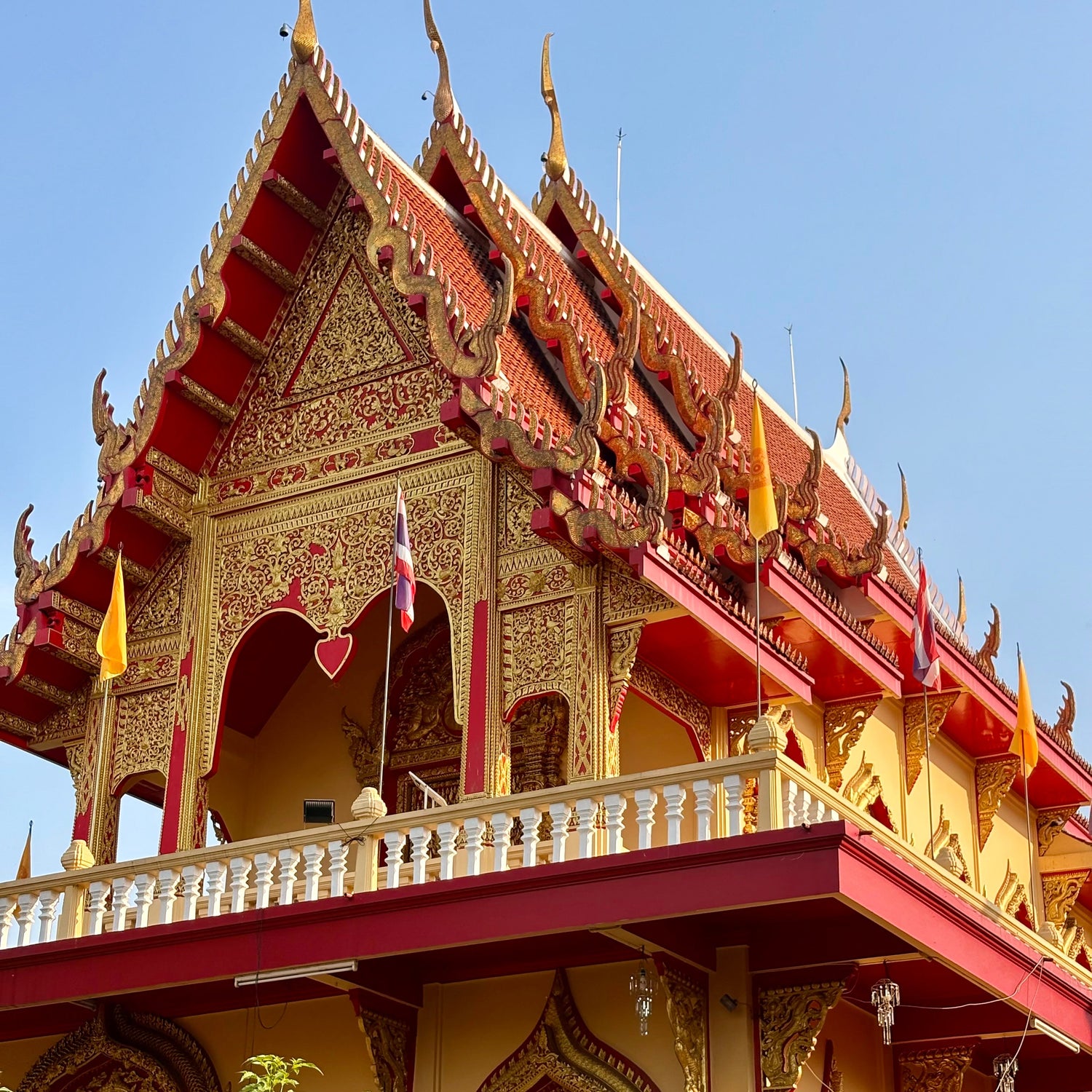 Decorative roof of a traditional building with intricate designs and colorful flags against a clear blue sky.