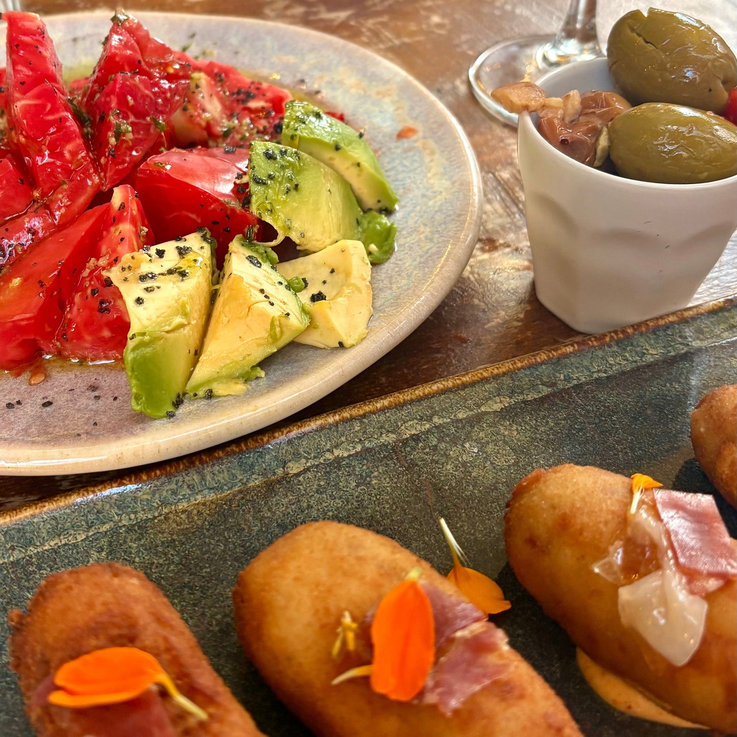 Spanish tapas with tomato, avocado, croquettes, and olives on a wooden table