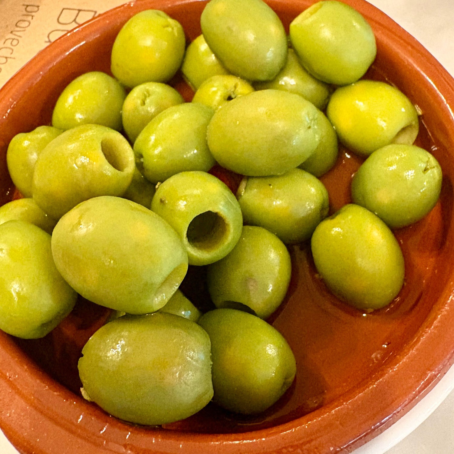 Green olives in a terracotta bowl on a marble surface