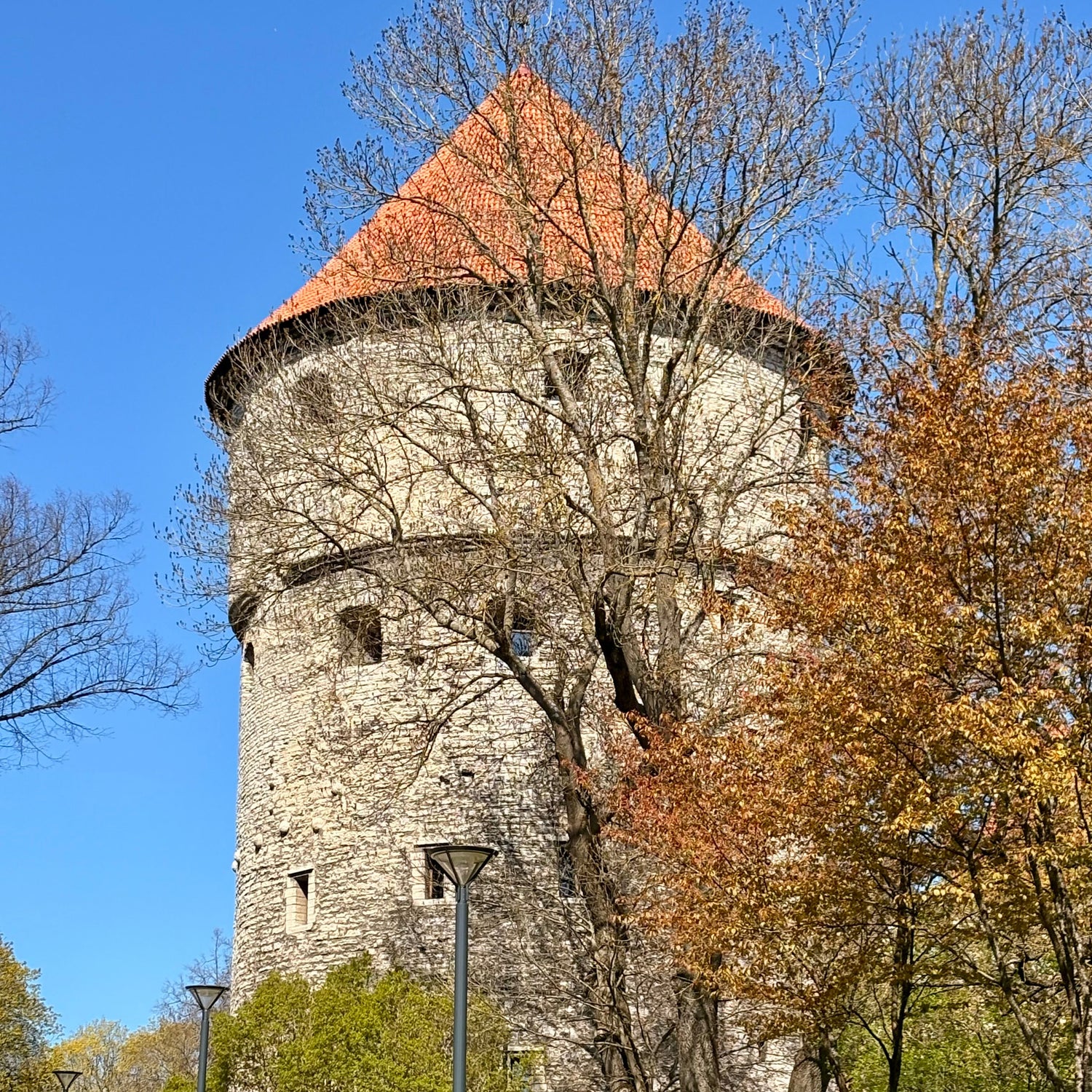 Stone tower with a red roof surrounded by trees and greenery on a clear day