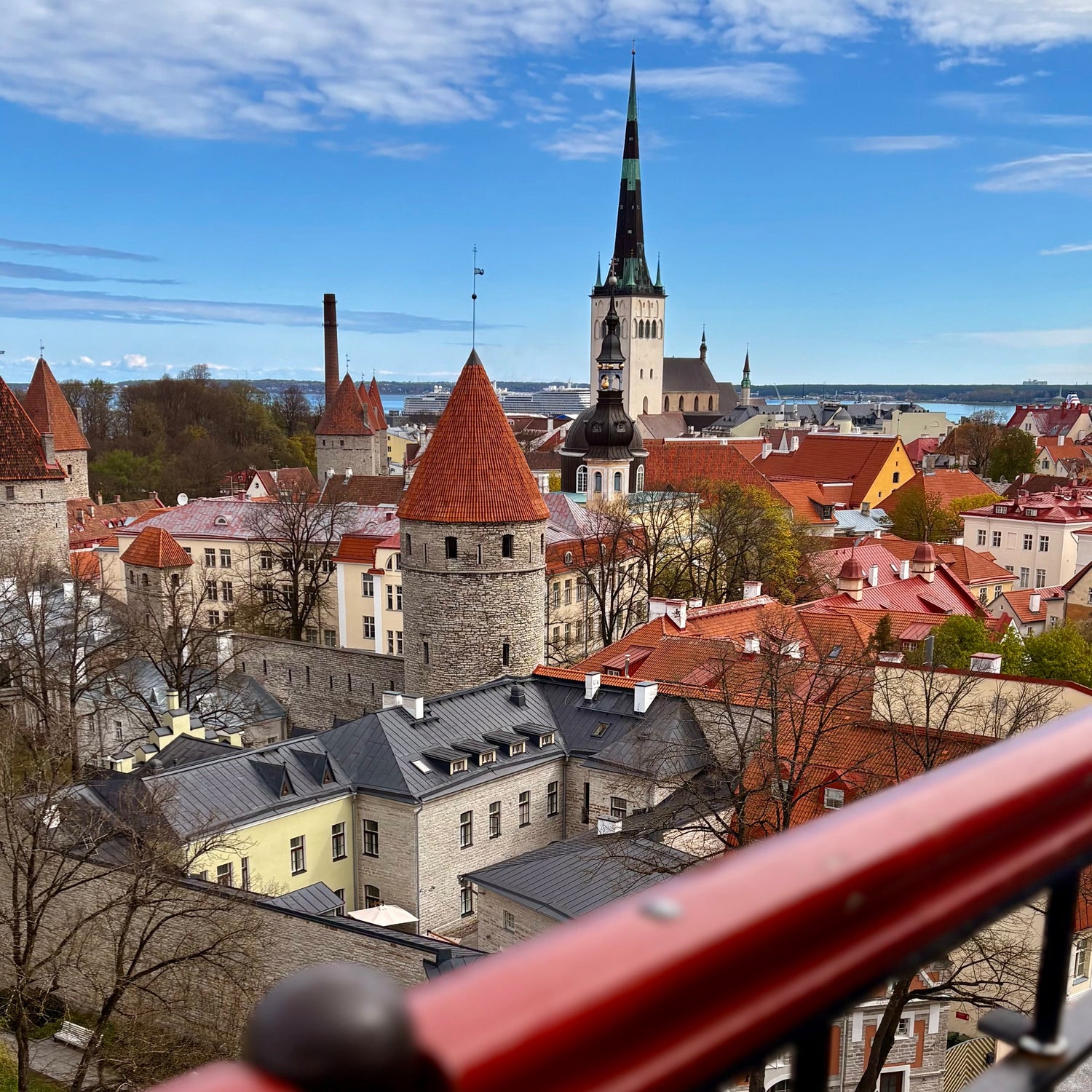 Cityscape with red-roofed buildings and a prominent church steeple under a blue sky.